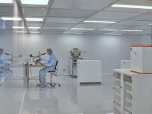 homme en combinaison stérile devant un microscope dans une salle blanche par Rosin Entreprise